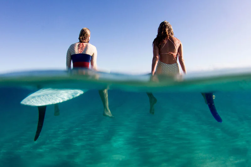 Over and under water shot of two surfers paddling out through clear turquoise water